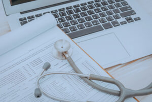 Stethoscope resting on medical documents next to a laptop