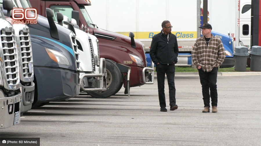 two men standing in front of semi trucks in a parking lot